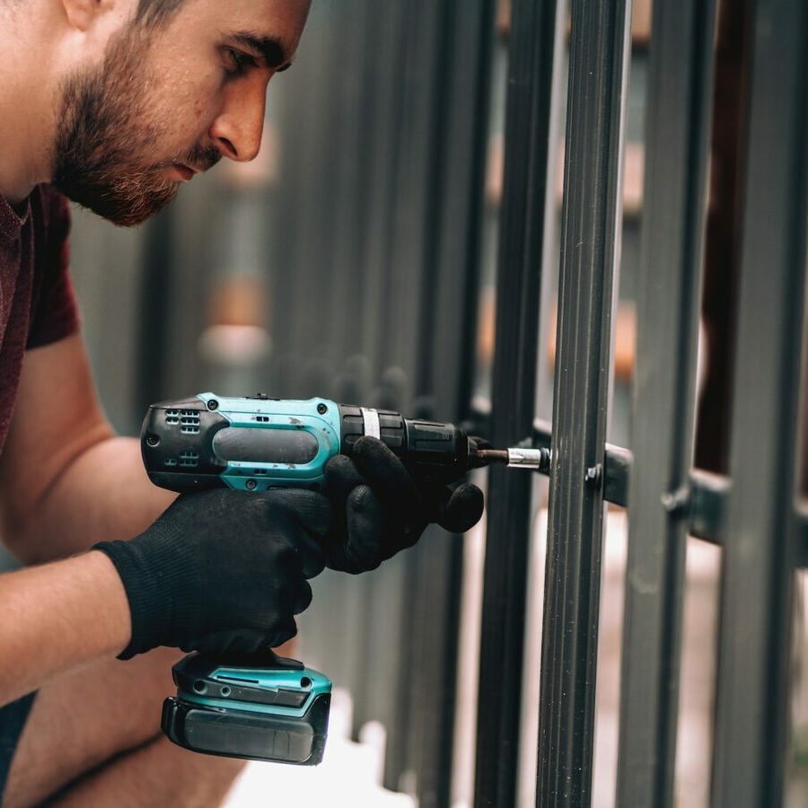 Close up of construction worker using screwdriver and drilling screws into metal fence