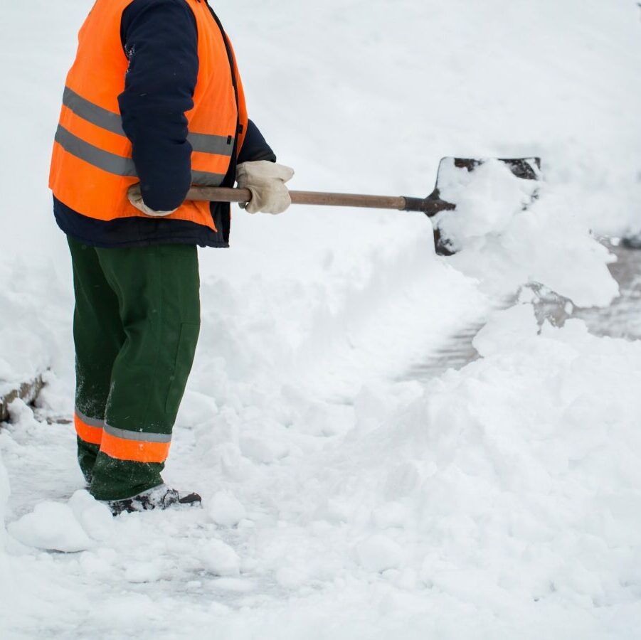 Mitarbeiter räument mit einer Schaufel den Schnee vom Gehweg
